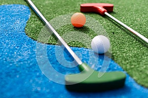 Mini-golf clubs and balls of different colors laid on artificial grass.