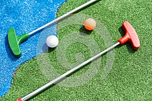 Mini-golf clubs and balls of different colors laid on artificial grass.