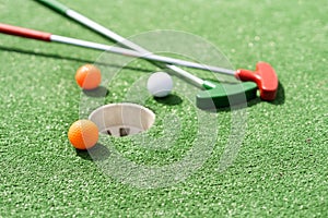 Mini-golf clubs and balls of different colors laid on artificial grass.