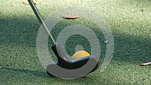 Mini golf. A green field covered with artificial turf, on which lies a yellow ball, which is hit with a golf club. Golf