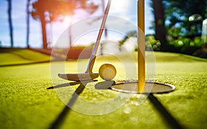 Mini Golf yellow ball with a bat near the hole at sunset photo