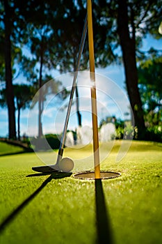 Mini Golf yellow ball with a bat near the hole at sunset