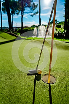 Mini Golf yellow ball with a bat near the hole at sunset