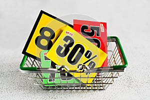 Mini grocery shopping basket with bright cards with a thirty percent discount sign and above. Conceptual image of a clear