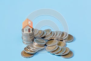 Mini house on stack of coins on a blue background. Concept of Investment property. Saving money, investing in real estate