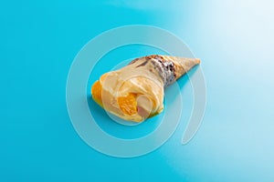Mini mango or orange flavor ice cream cone melting on blue
