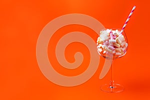 Mini marshmallows in a glass on a bright orange background. Multi-colored marshmallows in a glass