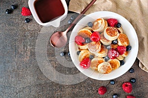 Mini pancake cereal with berries, overhead view table scene with a dark stone background and copy space