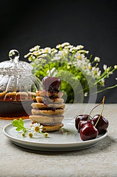 mini pancakes with fruit and varenie on a plate with cherries and camomiles in the background.