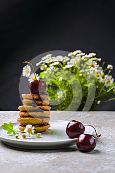 mini pancakes with fruit and varenie on a plate with cherries and camomiles in the background. Vertical orientation