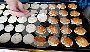 Mini pancakes frying on iron pan. Flipping half cooked pancakes around. Photographed in Tallinn, Estonia.