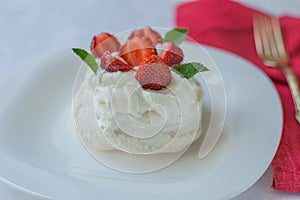 Mini Pavlova meringue cake with whipped cream, fresh strawberry and mint on white plate.Homemade meringues cookies. Australian cu