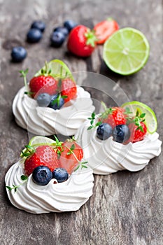 Mini Pavlova meringue cakes with berries and lime on rustic woo