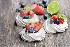 Mini Pavlova meringue cakes with berries and lime on rustic woo