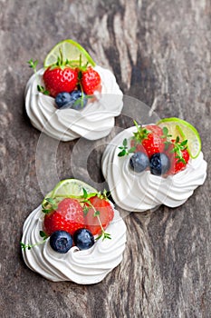 Mini Pavlova meringue cakes with berries and lime on rustic woo