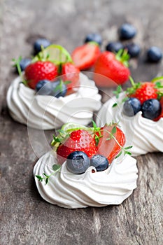 Mini Pavlova meringue cakes with berries and lime on rustic woo