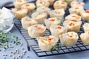 Mini quiche muffins with feta cheese, fried onion, thyme and red bell pepper, on a cooling rack, horizontal