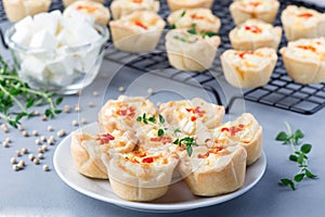 Mini quiche muffins with feta cheese, fried onion, thyme and red bell pepper, on a plate and cooling rack, horizontal