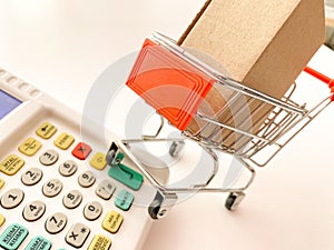 Mini shopping cart with a box and calculator isolated on a pink surface