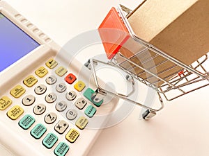 Mini shopping cart with a box and calculator isolated on a pink surface