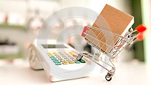 Mini shopping cart with a box and calculator isolated on a pink surface