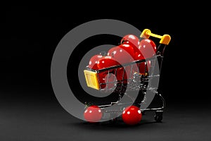 Mini shopping cart with cherry tomatoes on black background. Healthy eating and vegetarian food, cooking concept. selective focus