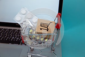 Mini shopping cart full of homeopathic remedies on laptop background. Homeopathy and internet online shopping.