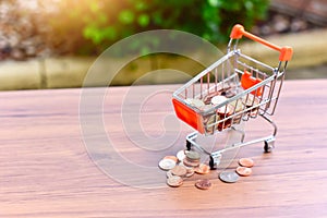 Mini Shopping Cart or Trolley and Glass Jar Filled with Coins Isolated on a Table as for Retail Business