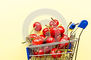 Mini shopping grocery cart full of fresh cherries Fresh berries on yellow background. Healthy summer food concept