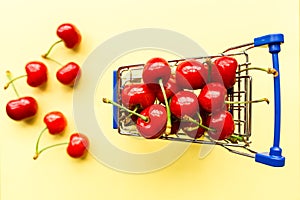 Mini shopping grocery cart full of fresh cherries. Fresh berries on yellow background. Healthy, summer food concept. Top