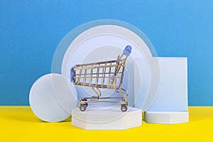Mini shopping trolley cart with geometric podium platforms on yellow and light blue background