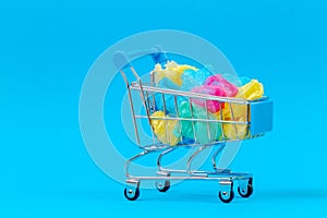 Mini shopping trolley full of colorful single use plastic bags on blue background