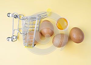 A mini shopping trolley with speckled chicken eggs and yolk on a neutral background