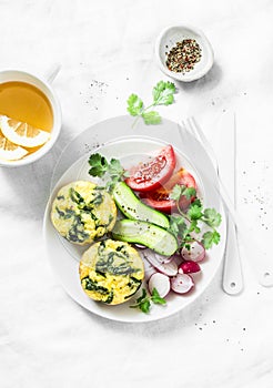 Mini spinach cheddar frittata, vegetables salad and green tea on light background, top view. Breakfast table