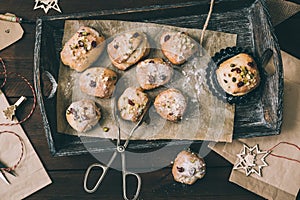 Mini stollen with sugar icing on a wooden tray, paper bags, scissors and gift ribbon on dark wood