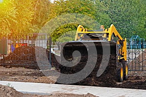 Mini tractor pours the soil out of the bucket, yellow excavator at work