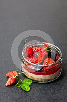 Mini wild forest berries cheesecake in a glass pot on black sto