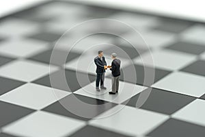 Miniature 2 people businessmen Shake hands on a chessboard with a chess piece on the back Negotiating in business. as background