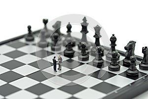 Miniature 2 people businessmen Shake hands on a chessboard with a chess piece on the back Negotiating in business. as background