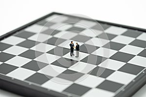 Miniature 2 people businessmen Shake hands on a chessboard with a chess piece on the back Negotiating in business. as background