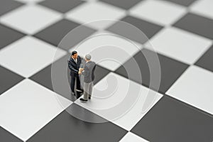 Miniature 2 people businessmen Shake hands standing on a chessboard with a chess piece on the back Negotiating in business. as