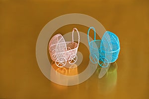 Miniature baby carriages isolated on a gold background. Pink and blue prams and copy space. Top view