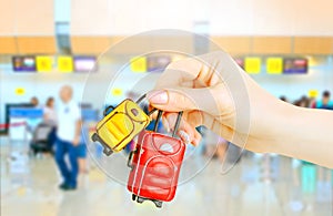 Miniature baggage in female hands on blurred background with airport check-In counters.