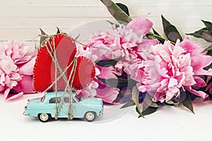 Miniature blue toy car carrying a heart and pink peonies on the