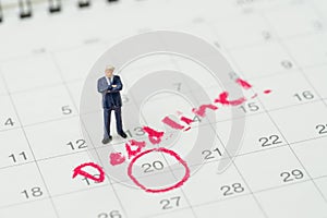 Miniature business man standing on desktop calendar with red circle on important date with handwriting deadline, goal or target