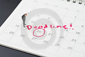 Miniature business man standing on desktop calendar with red circle on important date with handwriting deadline, goal or target