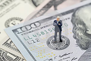 Miniature businessman leader standing and thinking on US Federal Reserve emblem on US dollars banknote as FED consider interest