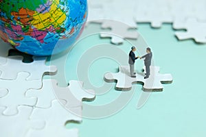 Miniature businessman make handshake partnership above jigsaw puzzle piece with globe