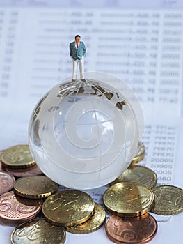 Miniature businessman stand on globe of glass, Euro coins and bo