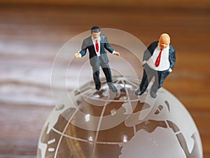Miniature businessman stand on globe of glass with wooden background. Business and idea concept.